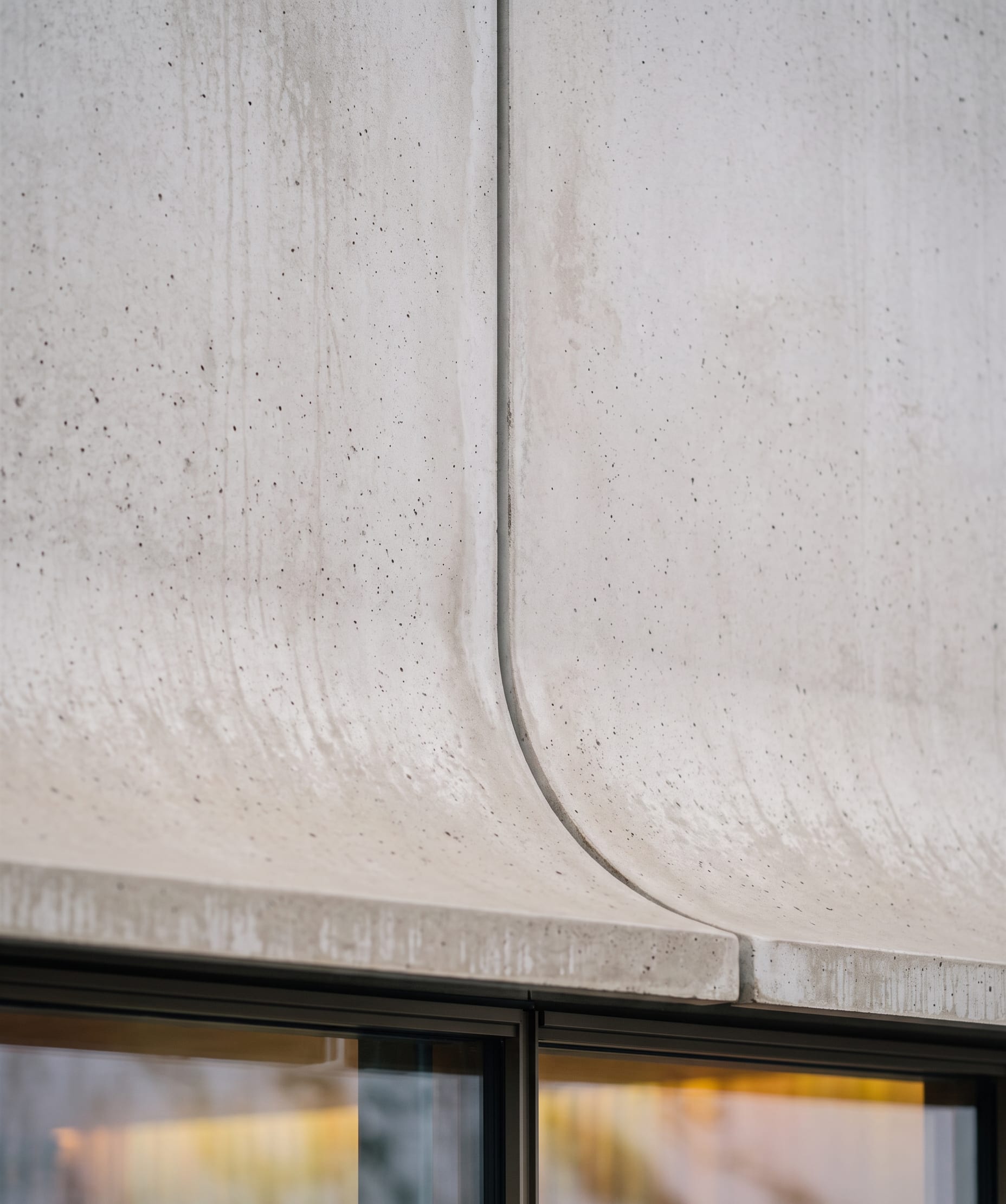 Close view of the curved concrete hood where two panels meet above the glazing