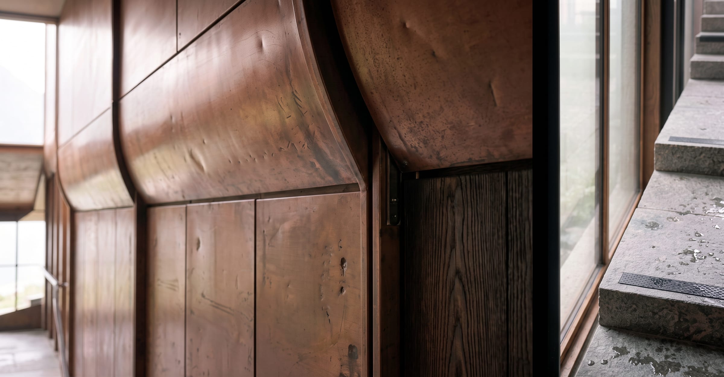 Copper panels curving at the corner of a passage, beside stone steps and glazing